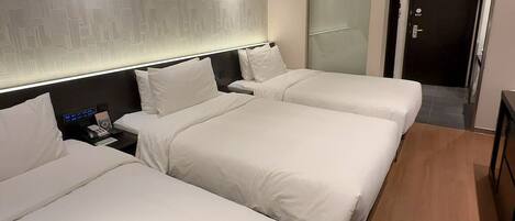 A hotel room with two beds, a bedside table, a wall-mounted light, and a door leading to another room.