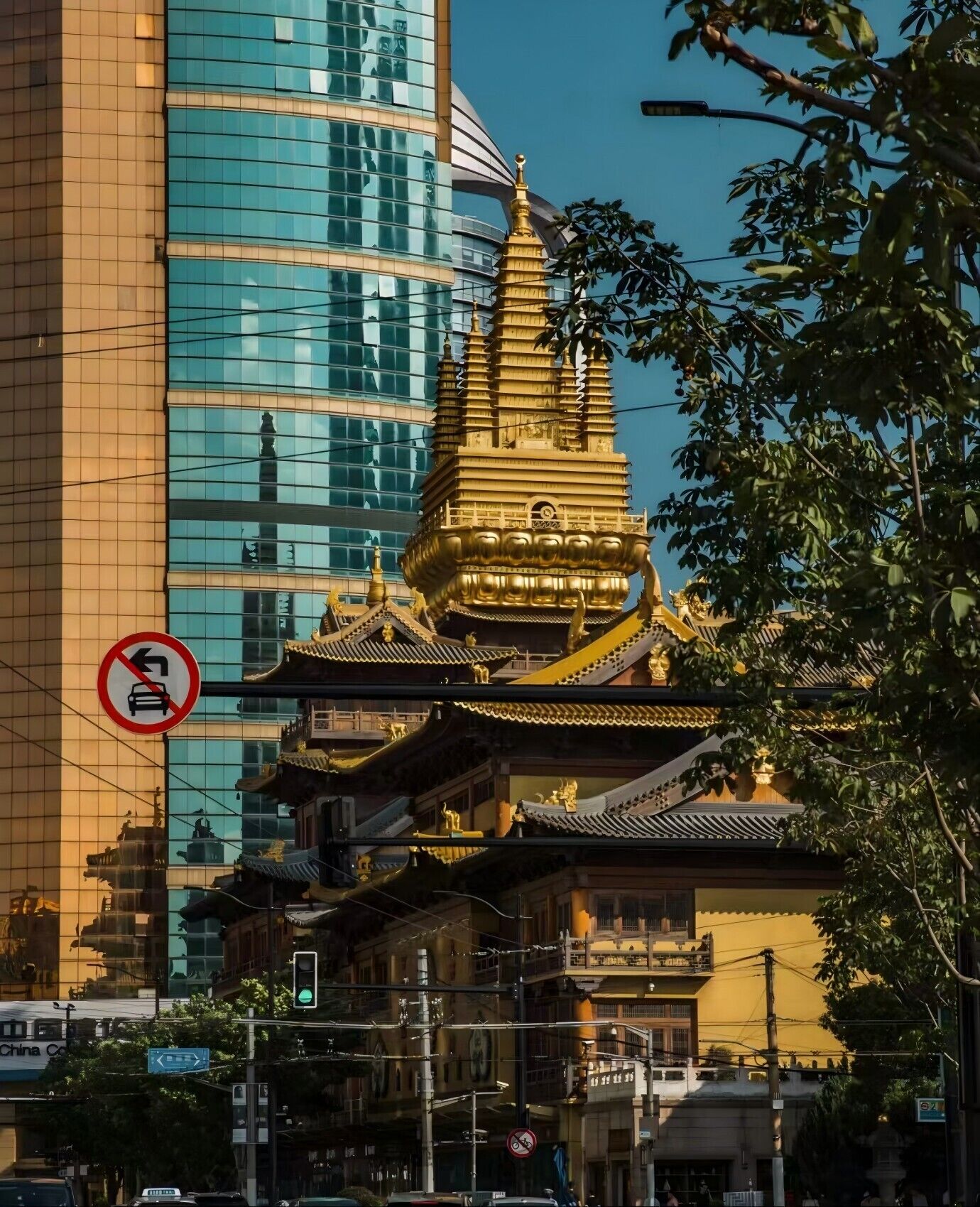 Un templo tradicional con tejados escalonados y detalles dorados, rodeado de edificios modernos y un cartel de prohibición de estacionamiento.