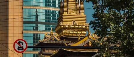Un templo tradicional con tejados escalonados y detalles dorados, rodeado de edificios modernos y un cartel de prohibición de estacionamiento.