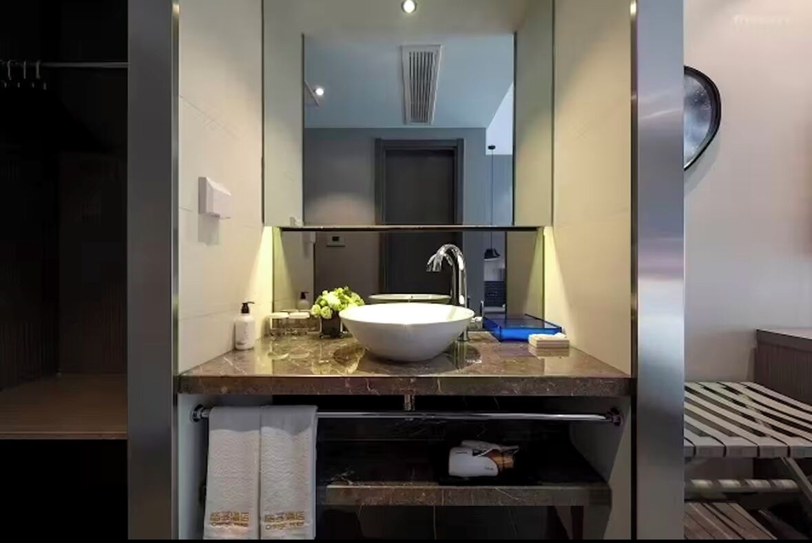 Un baño moderno con un espejo grande, un lavamanos blanco y un perchero para toallas.