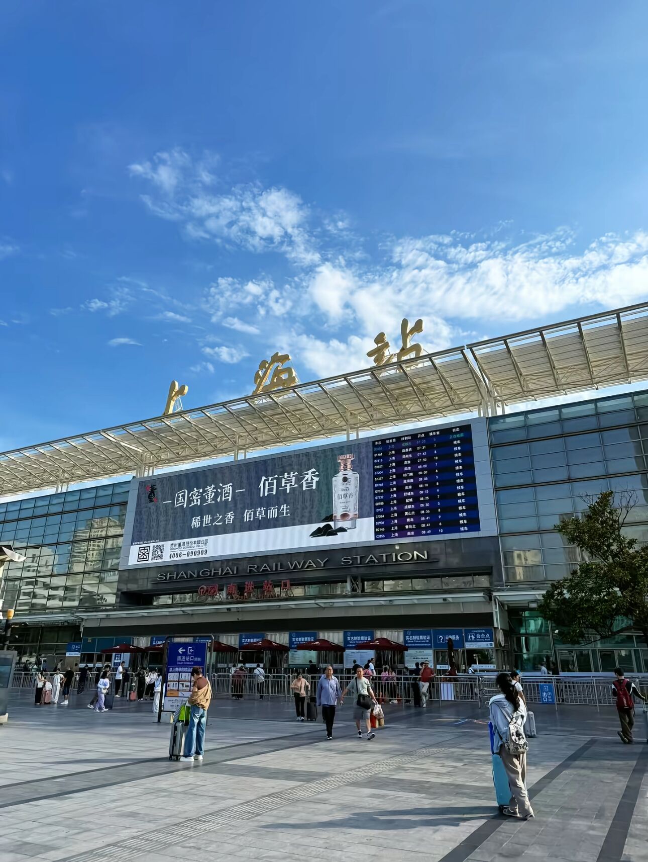 A train station with a large digital display, glass facade, and a clear sky.