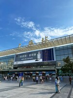 Una estación de tren con una gran pantalla digital, fachada de vidrio y cielo despejado.