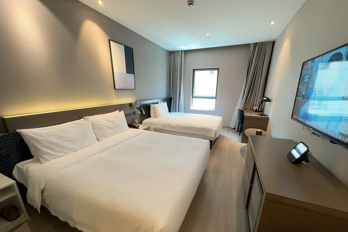 A hotel room with two beds, a desk, a TV, and a window.