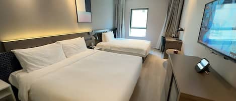 A hotel room with two beds, a desk, a TV, and a window.