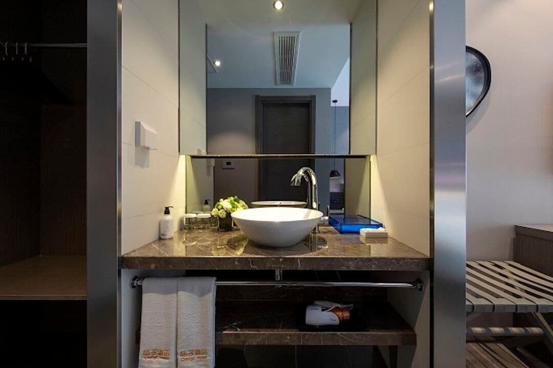 Une salle de bain moderne avec un grand miroir, un lavabo blanc et un porte-serviettes.