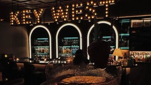 Un bar avec une enseigne au néon indiquant « KEY WEST » et une main tenant un verre.