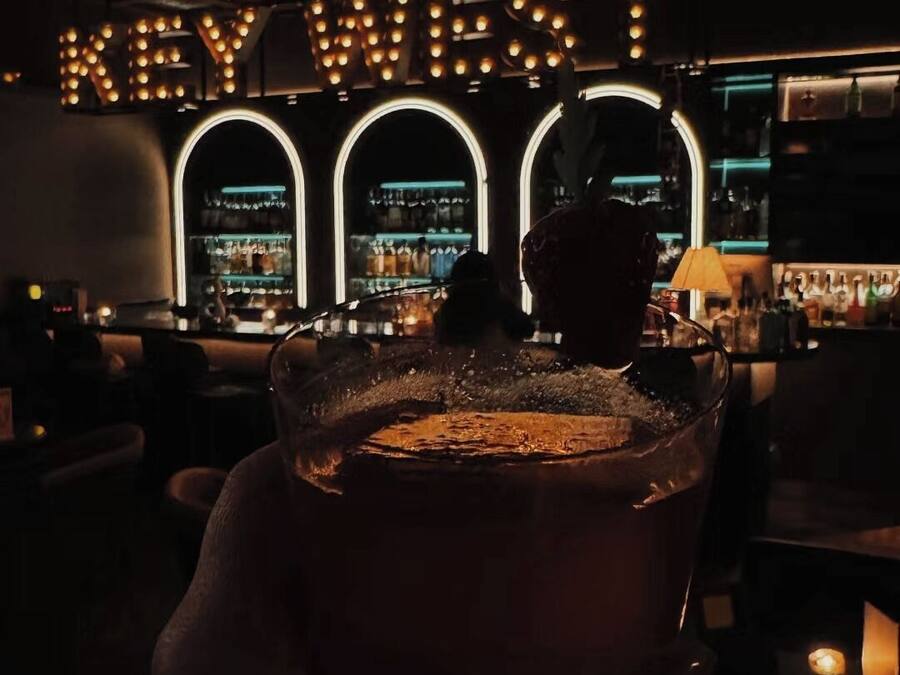 A bar with a neon sign reading "KEY WEST" and a hand holding a glass.