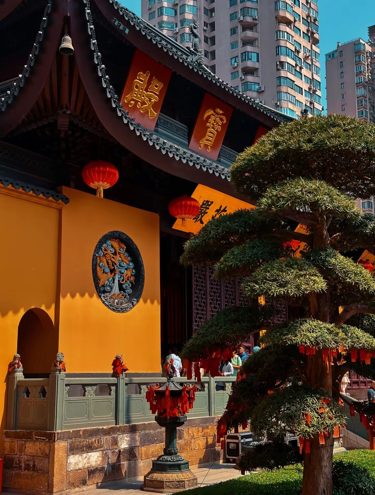 Un edificio tradizionale con decorazioni elaborate, un grande albero in primo piano e una vista chiara degli edifici circostanti.