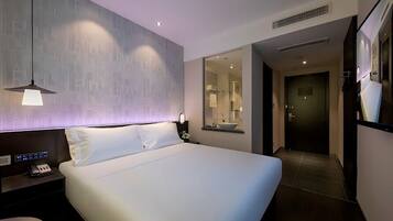 A modern hotel room with a large bed, a bedside table with a phone, a nightstand, a mirror, and a bathroom visible through an open door.