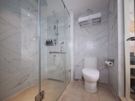 A modern bathroom with a glass-enclosed shower, a toilet, and a towel rack.