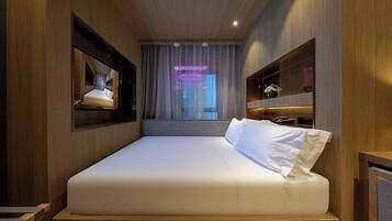A modern hotel room with a large bed, a TV mounted on the wall, and a neon sign in the background.