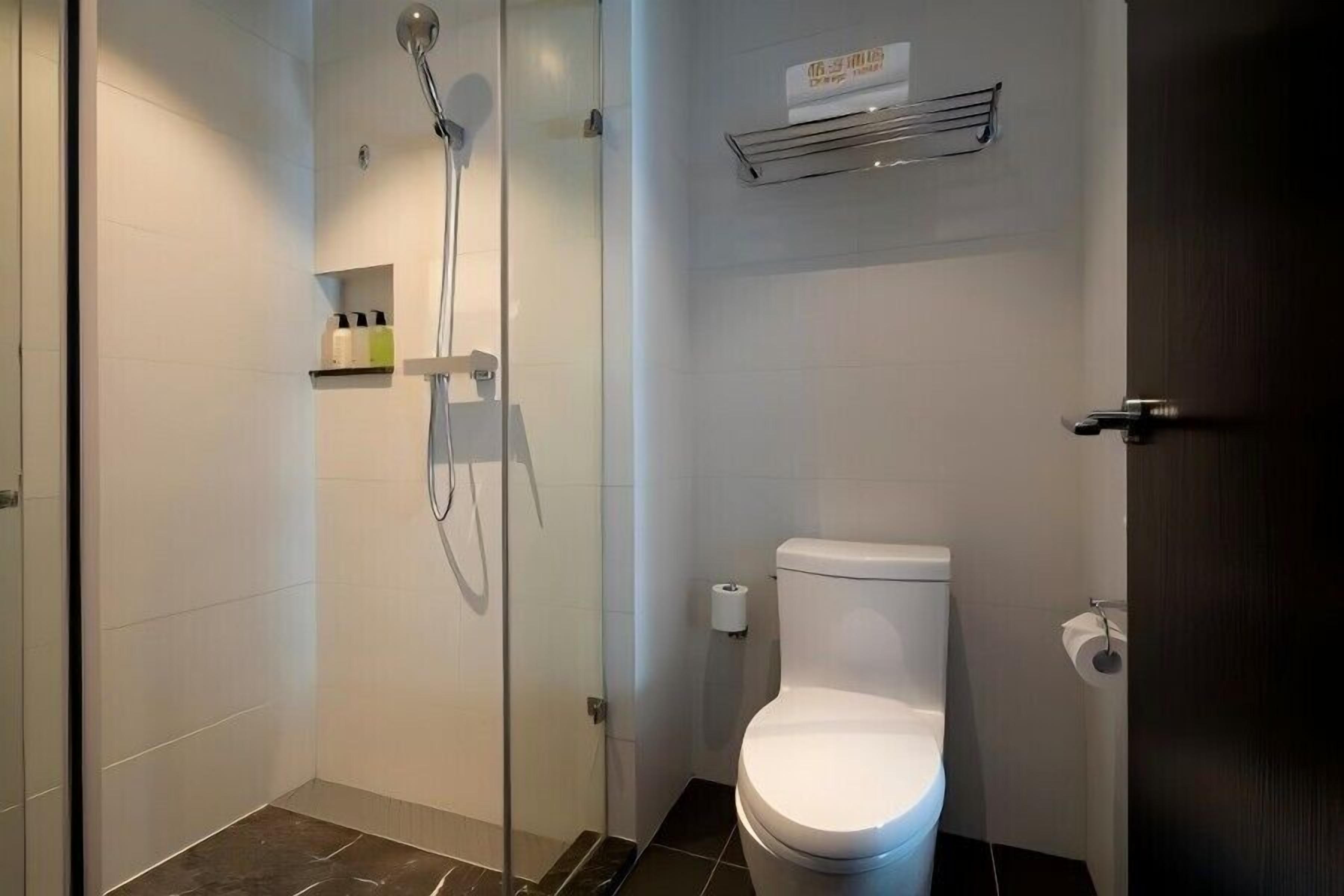 A modern bathroom with a glass-enclosed shower, a toilet, and a shelf with toiletries.
