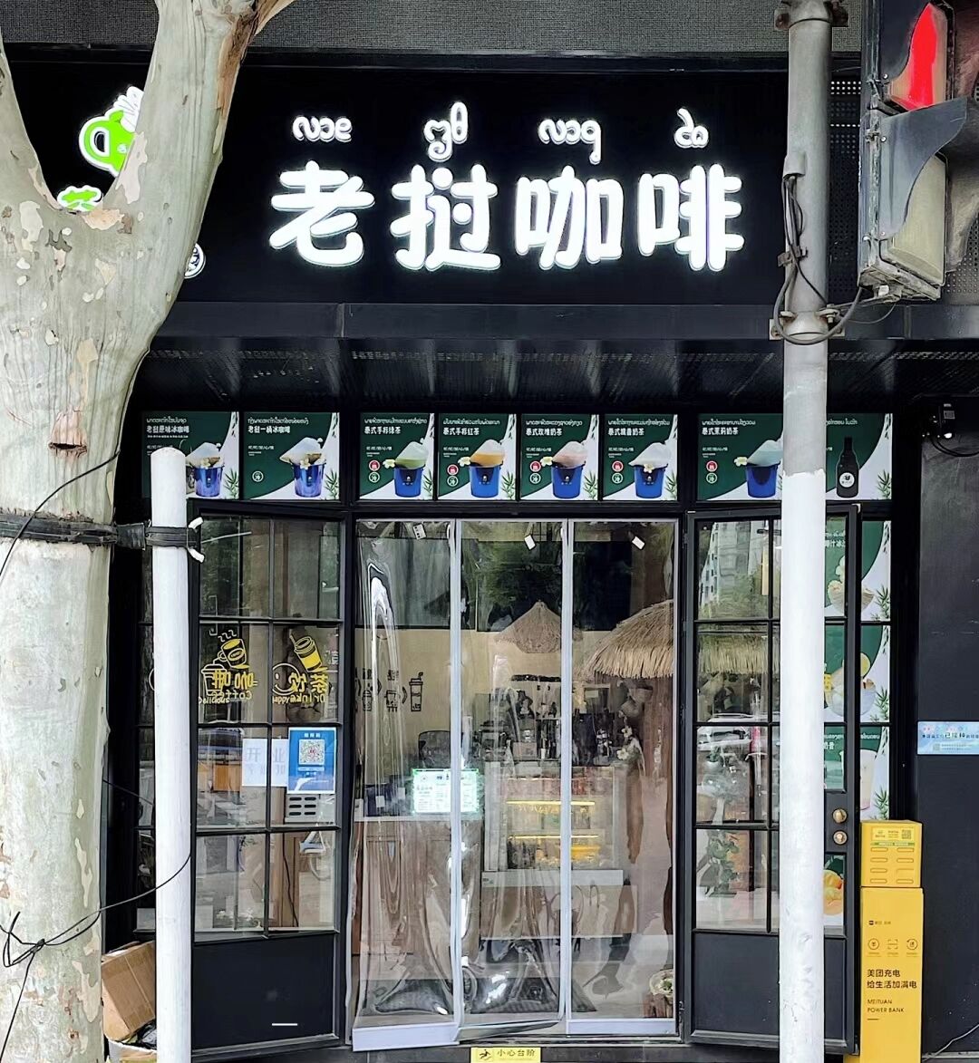 A storefront with a black sign and multiple beverage advertisements.