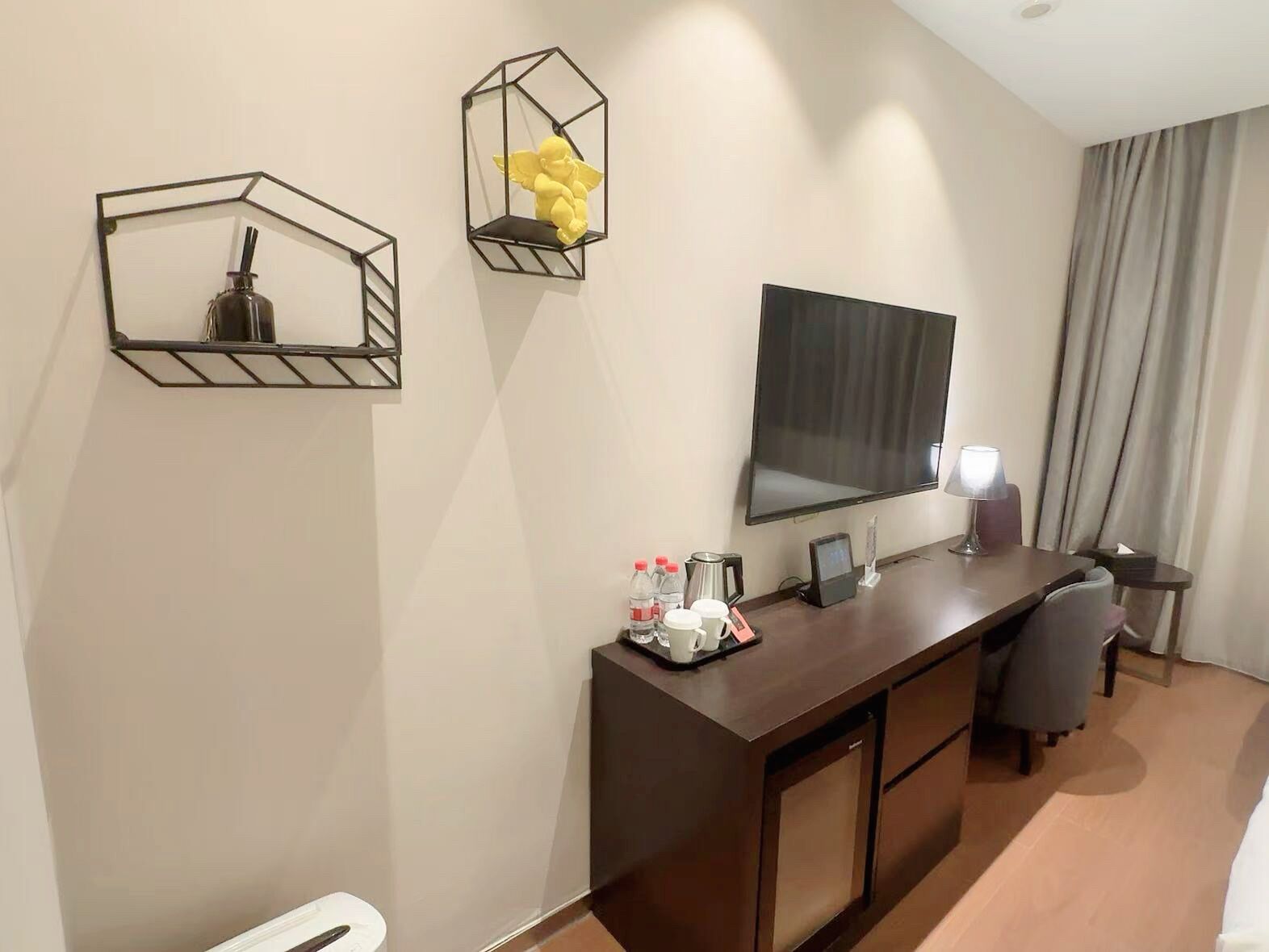 A hotel room with a dark wooden desk, a large mirror, and two geometric wall decorations.