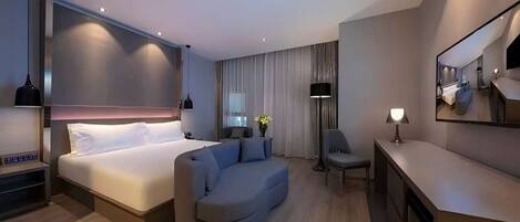 Ein modernes Hotelzimmer mit einem großen Bett, einer Sitzecke, einem Schreibtisch und einem Spiegel.