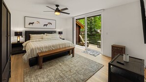 Een slaapkamer met een bed, bedlampen, een plafondventilator, een bankje, een tv-meubel en een schuifdeur die leidt naar een terras.