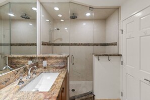A bathroom with a marble sink, a glass shower enclosure, and a white door.