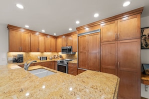 A kitchen with granite countertops, wooden cabinets, stainless steel appliances, and recessed ceiling lights.