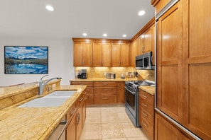 Una cocina moderna con armarios de madera, encimeras de granito y electrodomésticos de acero inoxidable, además de un cuadro de un paisaje montañoso.
