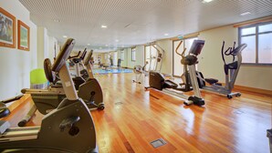 A gym with multiple exercise machines, wooden flooring, and large windows. - The Prime at The Residences Vilamoura (Loulé)