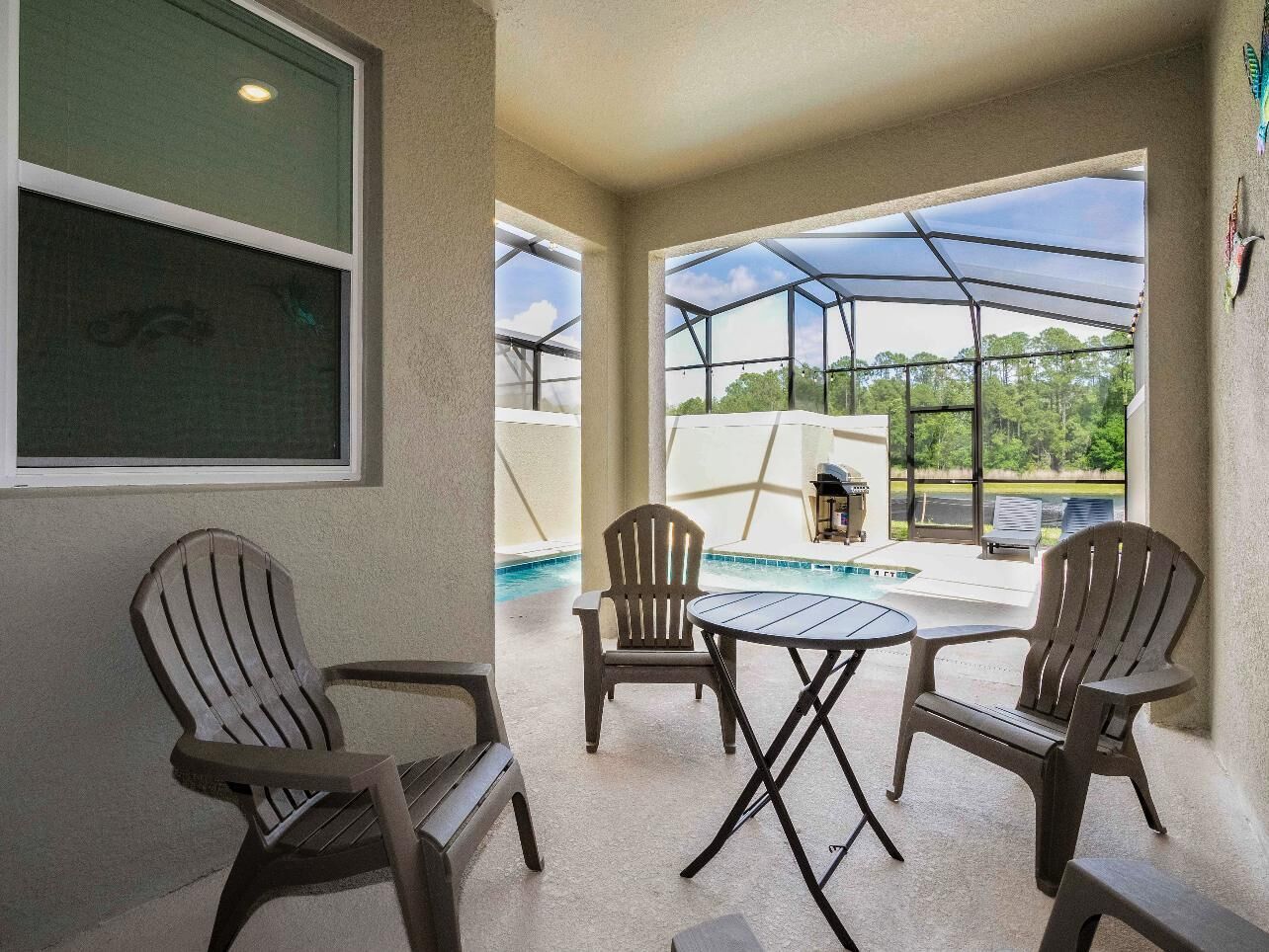 Un espacio de patio techado con sillas Adirondack, una pequeña mesa redonda y vistas a una piscina y vegetación.