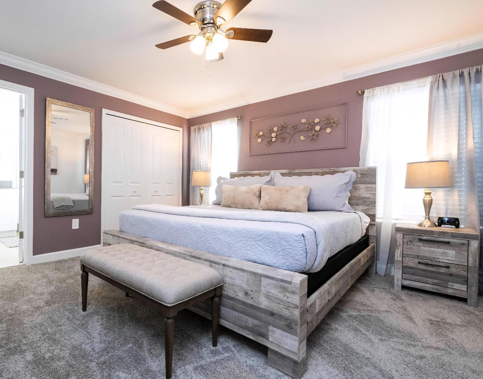 Een slaapkamer met een bed, een bankje, een nachtkastje, een plafondventilator en een decoratief wandobject.