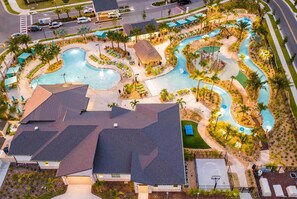 An aerial view of a resort with a large swimming pool, a water slide, and a tennis court.