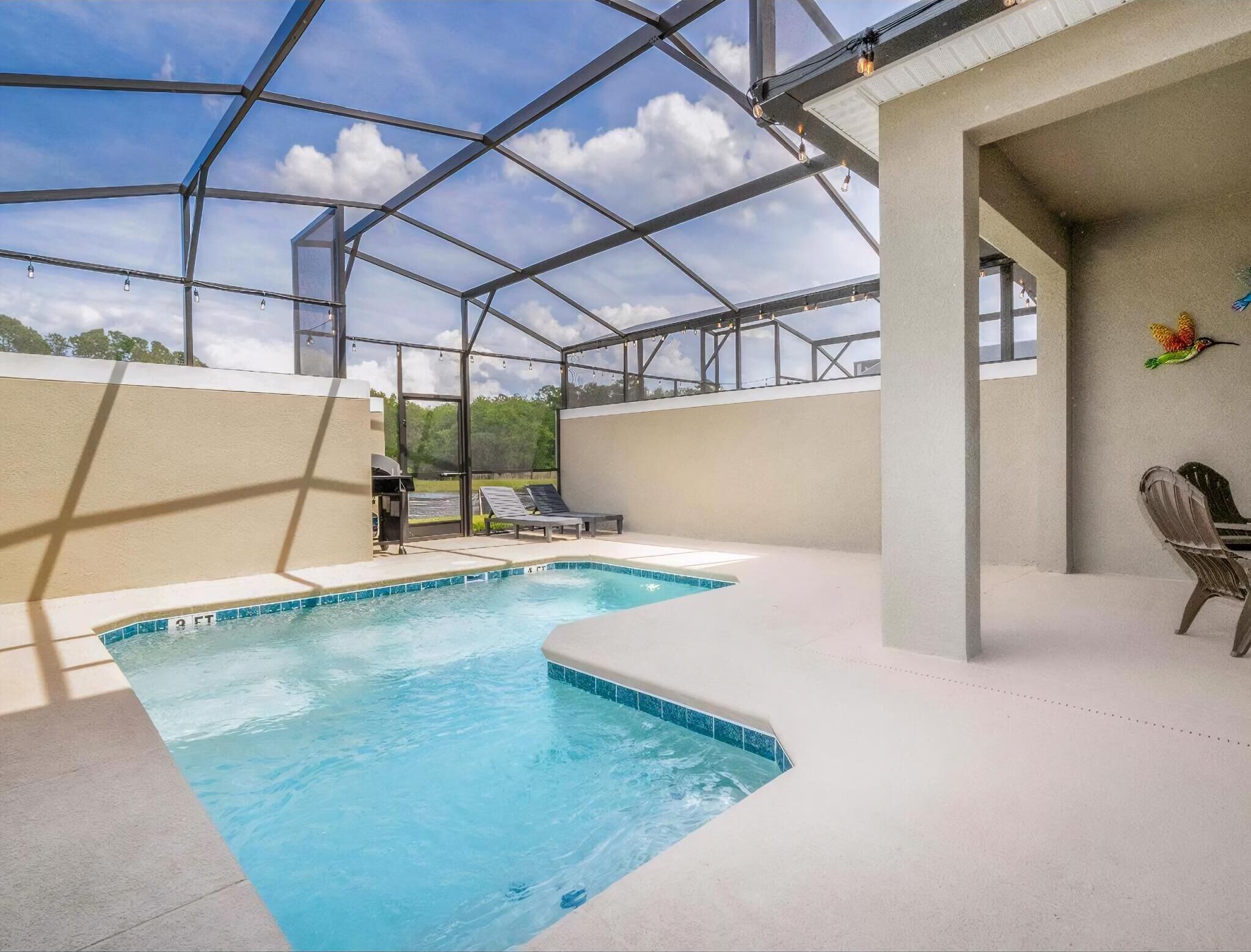 Una piscina exterior techada con techo de vidrio, sillas de descanso y zona de barbacoa.