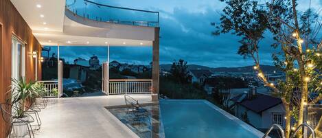 A modern outdoor pool area with a glass-enclosed deck, seating, and a view of the surrounding neighborhood.