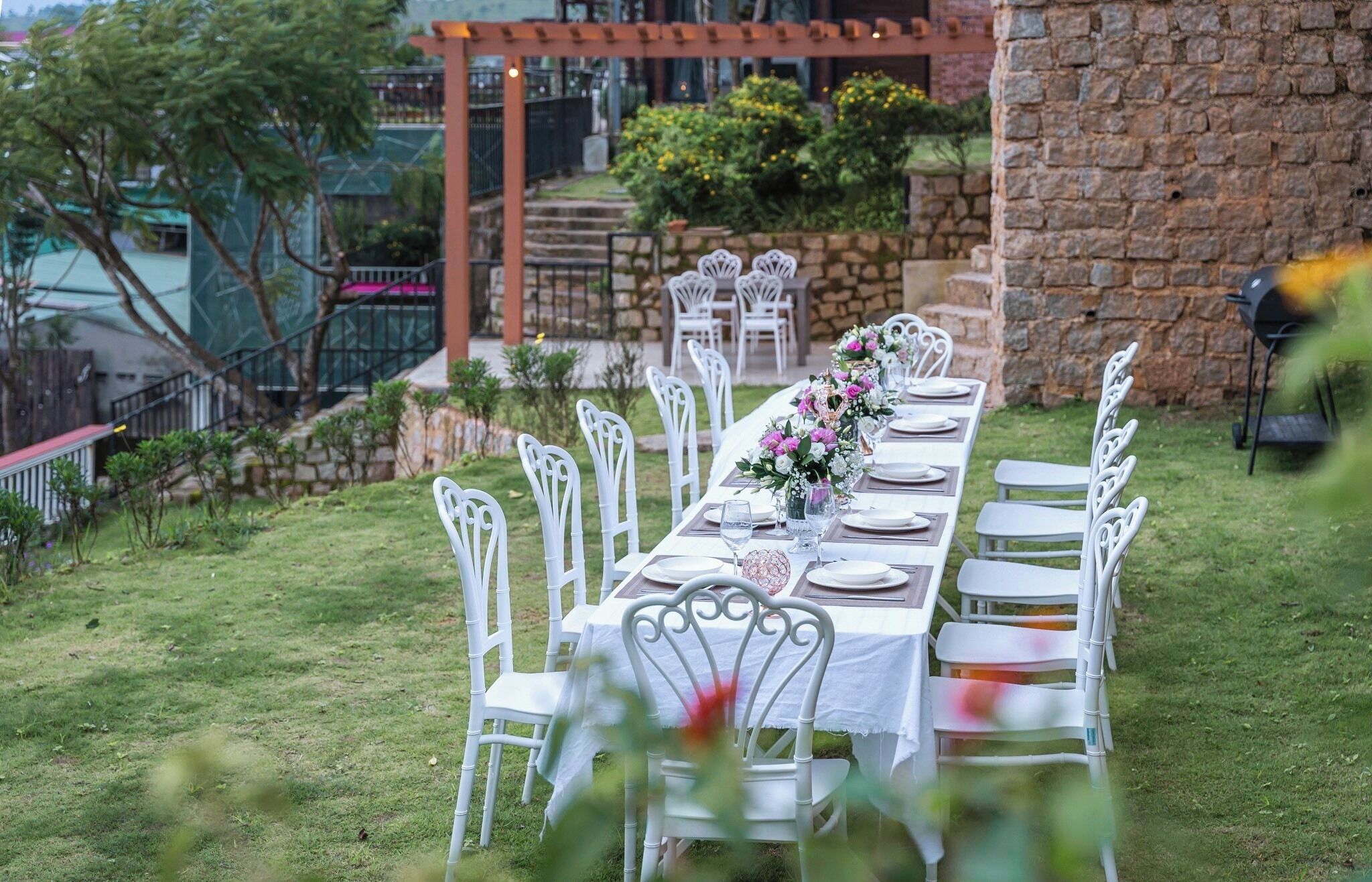 Un área de comedor al aire libre con una larga mesa dispuesta para una comida, rodeada de sillas blancas.