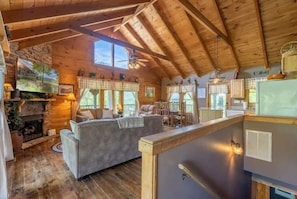 L’intérieur chaleureux d’un chalet avec un plafond en bois, une cheminée, un canapé et un coin cuisine.