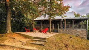 A covered outdoor seating area with red chairs and a wooden deck leading to a building with a metal roof. - Mountain VIEWS! Private, Hot Tub, & Game Room. (Sevierville)