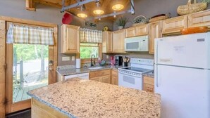 A kitchen with wooden cabinets, granite countertops, a microwave, a refrigerator, and a window with a view of greenery. - Mountain VIEWS! Private, Hot Tub, & Game Room. (Sevierville)