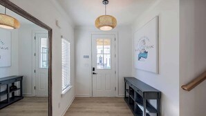 A hallway with a wooden floor, a white door, a console table, and a wall-mounted sign. - Sleeps 16 - GAME ROOM, POOL, Perfect for Families (Orange Beach)
