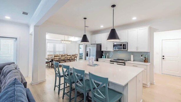 A modern kitchen with white cabinets, a central island with bar stools, and pendant lighting. - Sleeps 16 - GAME ROOM, POOL, Perfect for Families (Orange Beach)