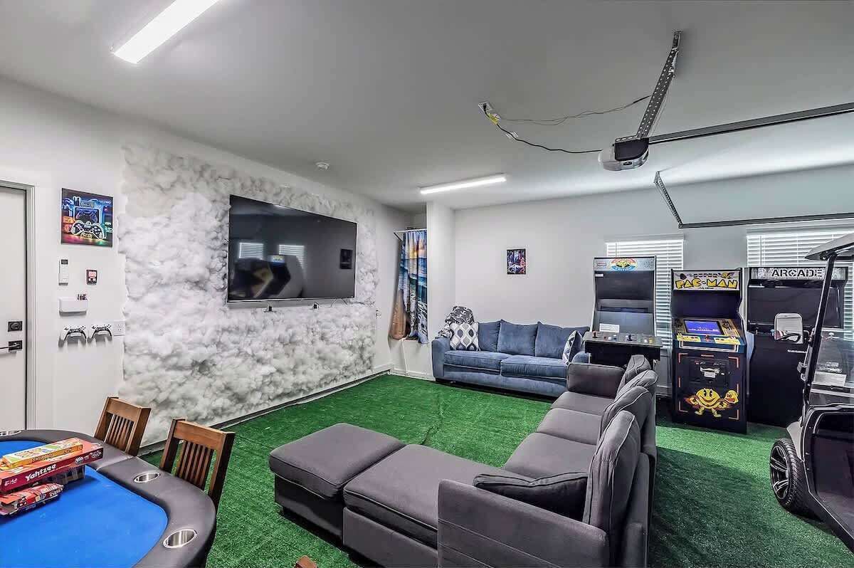 A living room with a pool table, a sofa, and arcade games.