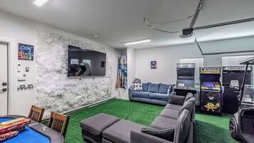 A living room with a pool table, a sofa, and arcade games.