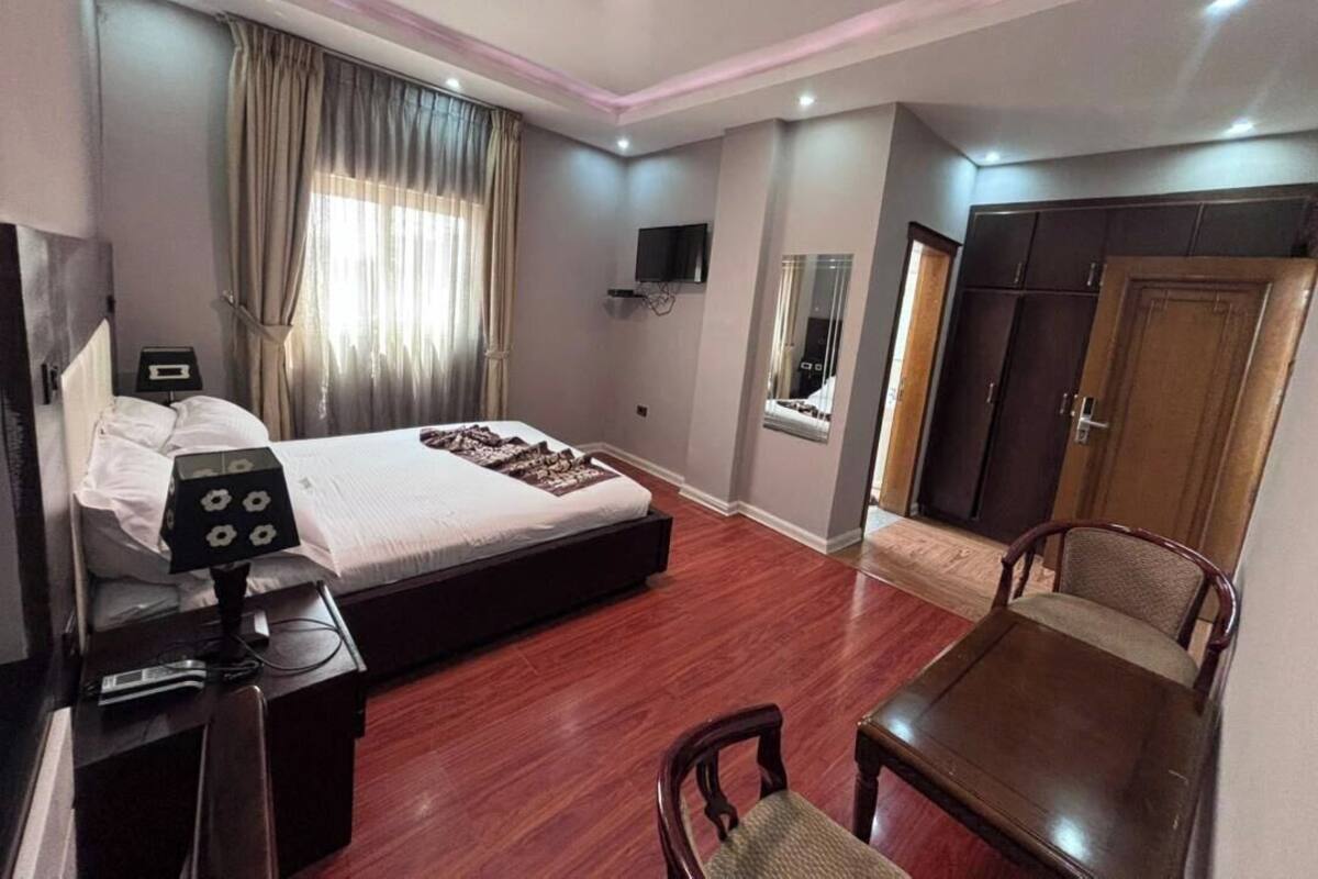 A hotel room with a bed, a desk, a chair, a TV, a wardrobe, and a window with curtains.