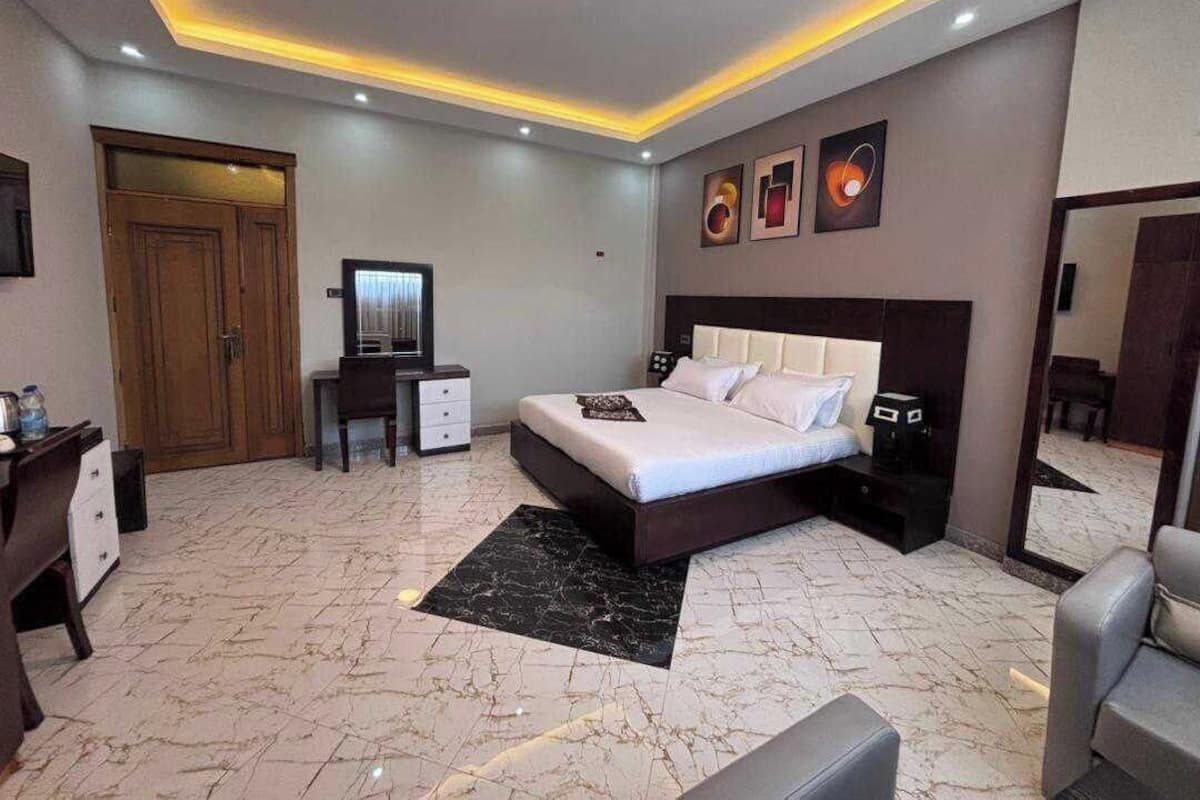 A modern bedroom with a large bed, a desk, a chair, and a wardrobe.
