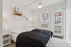 Een slaapkamer met een bed, nachtkastjes, een decoratie van een schip, een raam met uitzicht en een deur.