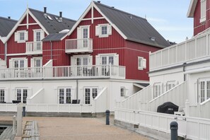Een rij rode en witte gebouwen met balkons, een grindpad en een houten hek.