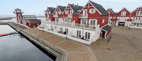 A row of red and white buildings with balconies, a dock, and a water body.