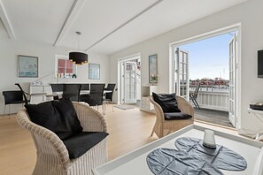 Ein großzügiger Wohnbereich mit Rattanmöbeln, einem Esstisch und einer großen offenen Tür, die auf einen Außenbalkon führt.