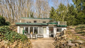 A two-story cabin with a balcony, surrounded by a stone wall and a wooden fence.