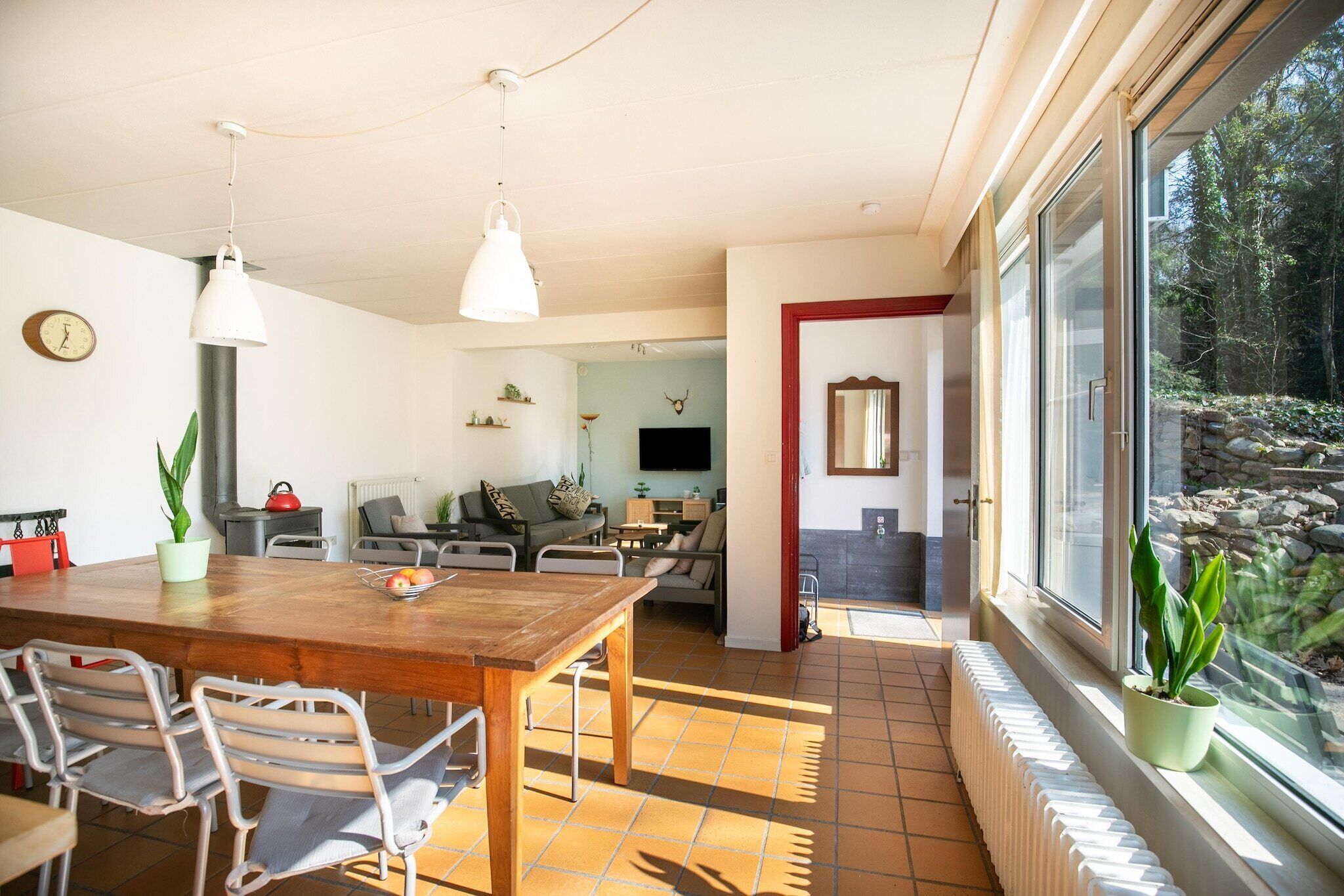 A spacious living area with a wooden dining table, chairs, and a TV. There are potted plants and a fireplace.