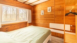 A wooden-paneled bedroom with a bed, a radiator, and two framed pictures on the wall.
