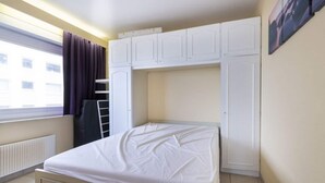 A bedroom with a bed, white wardrobe, and a window with curtains. - Apartment Middelkerke with Sea View (MIDDELKERKE)
