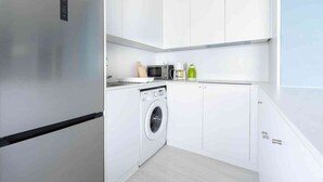 A modern kitchen with white cabinetry, a stainless steel refrigerator, a washing machine, a microwave, and a coffee maker. - Apartment Middelkerke with Sea View (MIDDELKERKE)