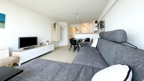 Una sala de estar moderna con un sofá gris, un televisor de pantalla plana y una zona de comedor con una mesa y sillas.