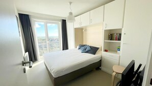 Un dormitorio con cama, escritorio, silla y ventana con cortinas.